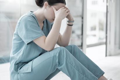 Woman in scrubs sitting on the floor, head in hands