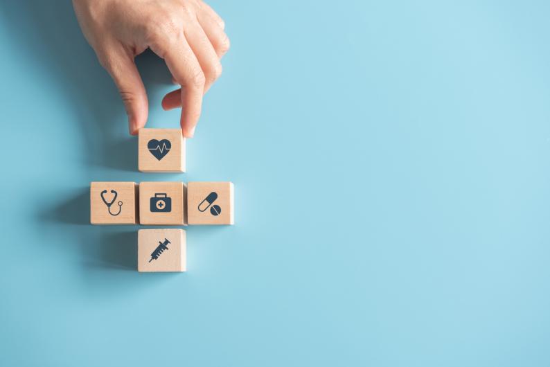 five wood squares with syringe, pills, heart, stethoscope and medical bag